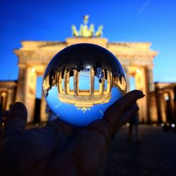 Close-up of hand holding illuminated building against blue sky