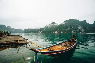 Boat moored by pier in lake against sky