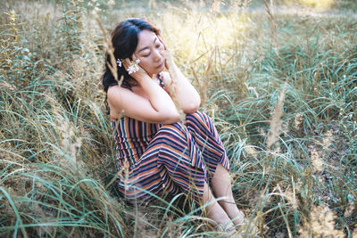 Side view of young woman sitting on field