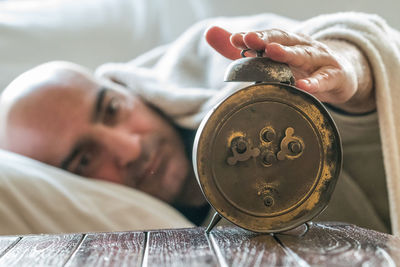 Man touching alarm clock while relaxing on bed at home