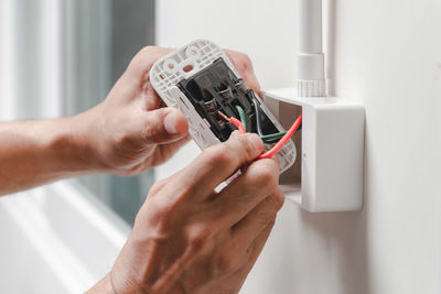 Cropped hands of male electrician repairing electrical outlet on wall