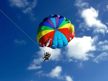 Low angle view of people paragliding against sky