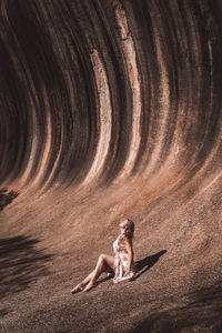 Side view of woman sitting against wall