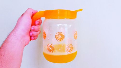 Cropped hand holding jug against white background