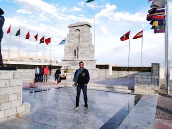 Full length portrait of man standing amidst flags against sky