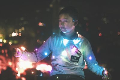 Boy holding illuminated string lights at night