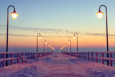 Illuminated street light by sea against sky during sunset