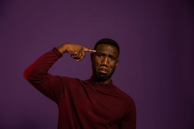 Portrait of young man holding eyeglasses against gray background