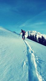 Low angle view of hiker climbing on snow covered mountain against blue sky