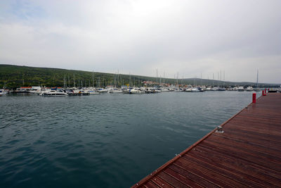 Sailboats moored at harbor on sea against cloudy sky