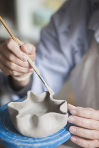 Midsection of senior female potter using paintbrush on vase at workshop