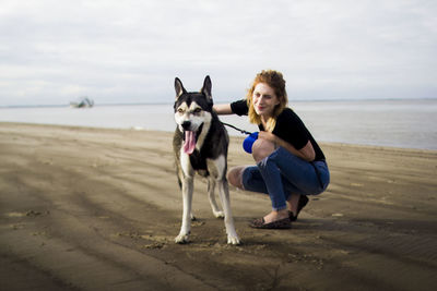 Portrait of woman with dog on beach against sky