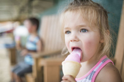 Young cute girl happily licking pink ice cream on summer day.