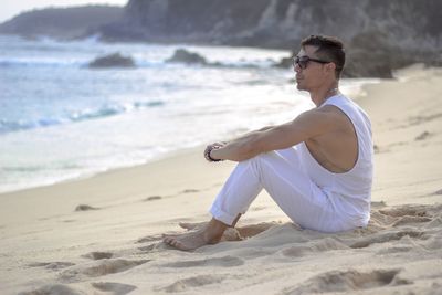 Man wearing sunglasses sitting on sand at beach