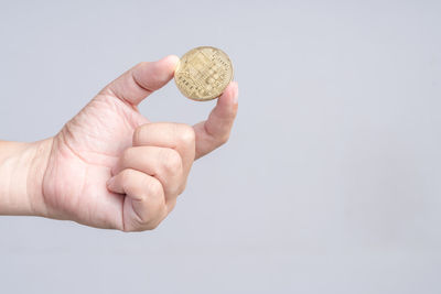 Cropped image of hand holding coin against white background