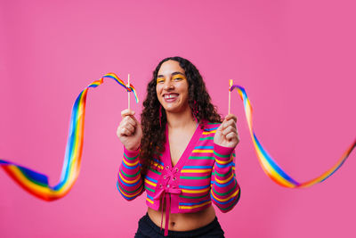 Portrait of young woman with arms raised standing against yellow background