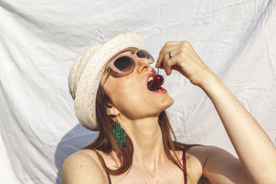 Close-up of woman wearing hat eating cherry against curtain
