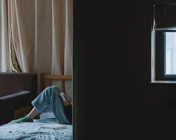 Low section of person reading book while sitting on bed at home