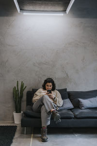 Young businesswoman using smart phone sitting on sofa in creative office