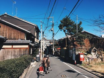 Rear view of man with baby carriage walking on road against blue sky