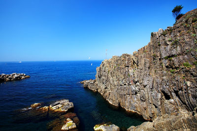 Rocks by sea against clear blue sky