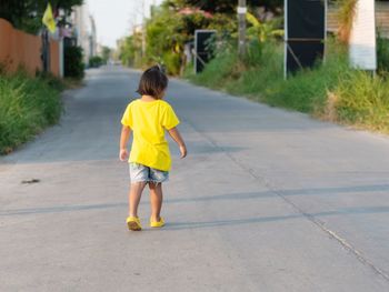 Rear view of boy walking on footpath in city