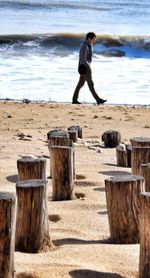 Man walking by wooden post at beach