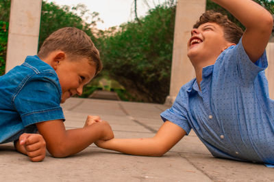 Friends arm wrestling while lying outdoors