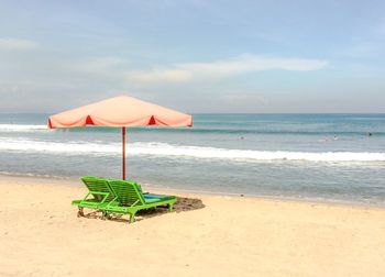 Lounge chairs below parasol at beach against sky