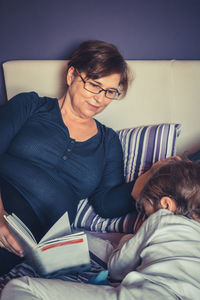 Grandmother reading book for grandson on bed