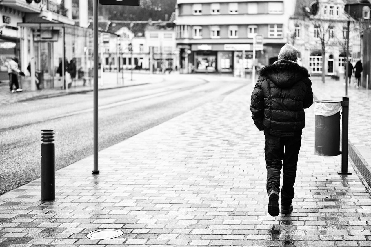 building exterior, walking, city, architecture, rear view, street, full length, built structure, city life, lifestyles, men, person, sidewalk, casual clothing, leisure activity, incidental people, cobblestone, standing