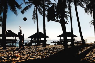 Silhouette woman playing with ball on beach against sky