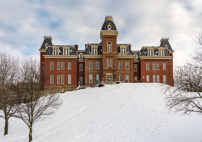 Snow covered field by building against sky