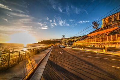 Road by bridge in city against sky during sunset