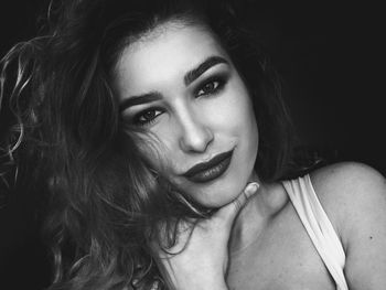 Close-up portrait of smiling young woman against black background