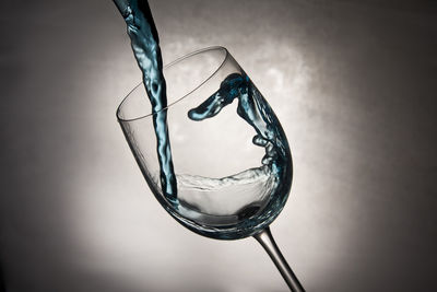 Close-up of drink being poured in wineglass against gray background