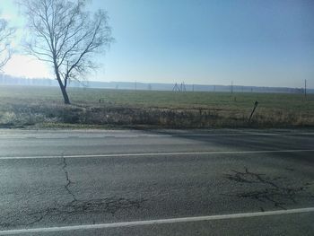 Road by bare trees on field against clear sky