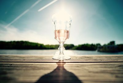 Close-up of wineglass on table against lake