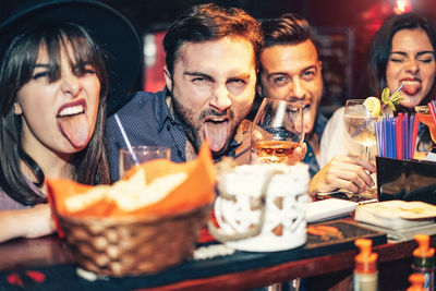 Portrait of friends with woman sticking out tongue in restaurant at night