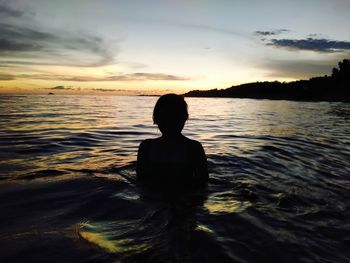 Rear view of silhouette woman against sea during sunset