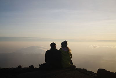 Rear view of people sitting on rock against sky