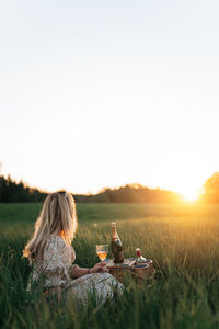 Young woman drinking wine while sitting outdoors during sunset