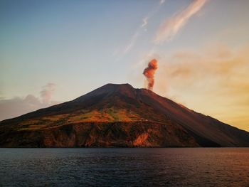 Scenic view of volcanic mountain by sea against sky during sunset