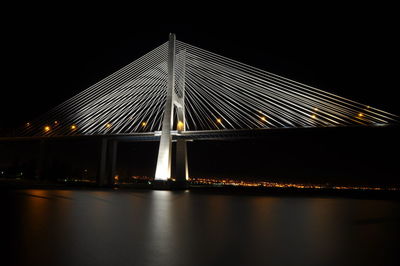 Illuminated bridge over river against sky at night