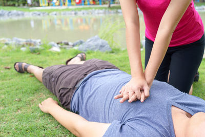 Midsection of woman giving cpr to unconscious victim lying on field