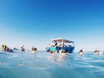 People swimming in pool against clear blue sky