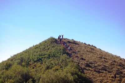 People walking on mountain against clear blue sky