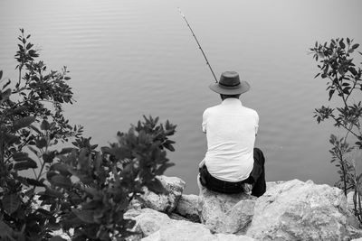 Rear view of man sitting on rock against calm lake