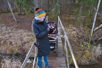 Woman with baby standing on footbridge using smart phone in park