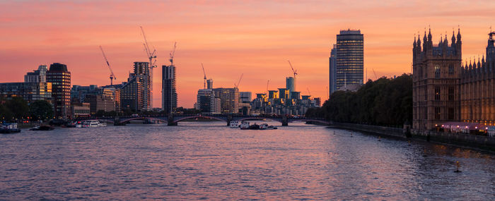 Bridge over river by buildings in city against sky during sunset